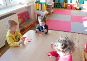 Widok na troje dzieci, które siedzą przy stolikach i sklejają papierowe serduszka